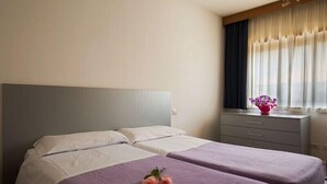 A hotel room with two beds, a bedside table with a vase of flowers, and a window with sheer curtains. - Residence Capitol (Trento)