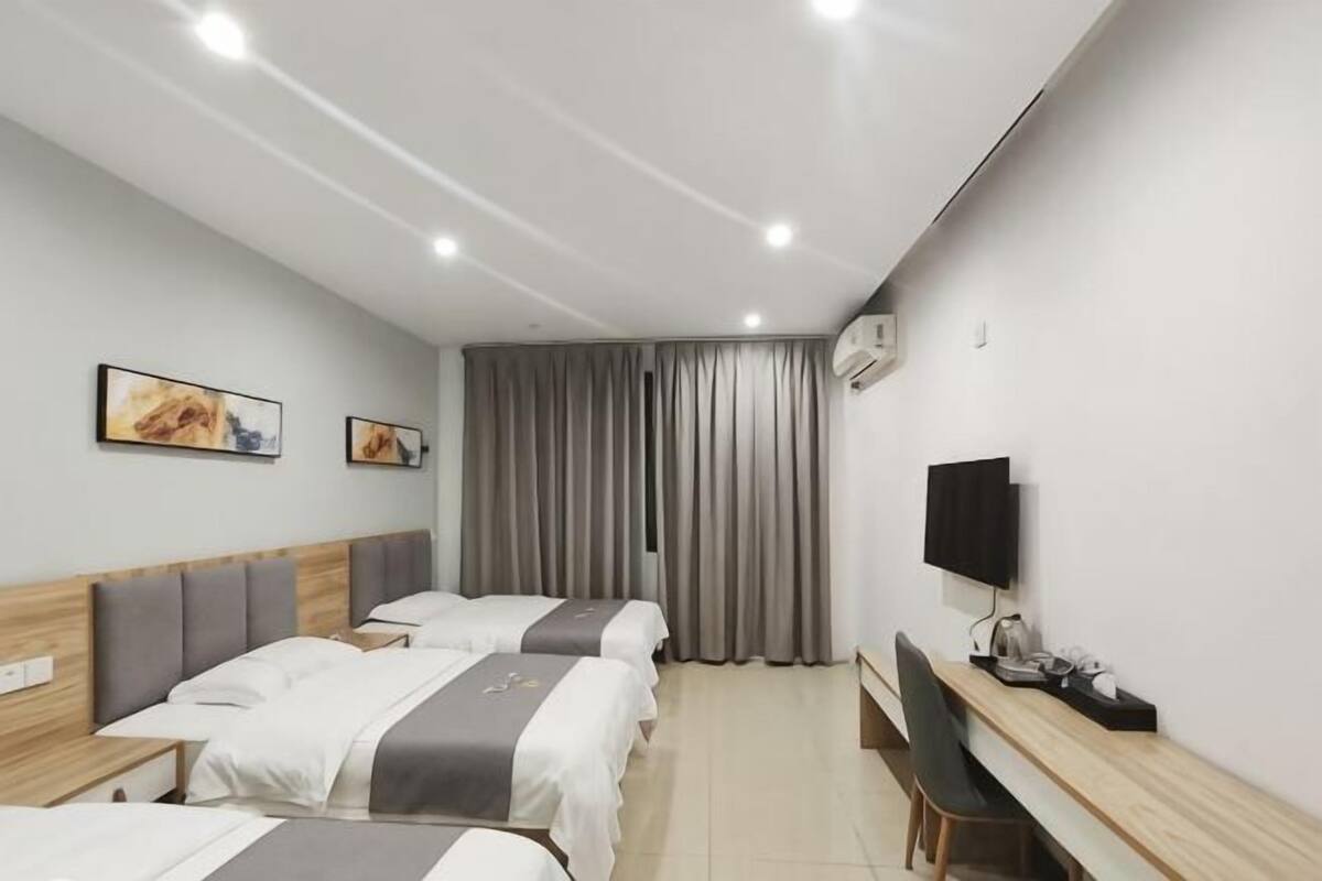 Habitación de hotel con tres camas, un escritorio, un televisor y dos cuadros en la pared.