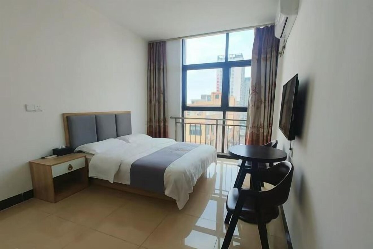 A hotel room with a bed, bedside table, chair, TV, and a balcony with curtains.
