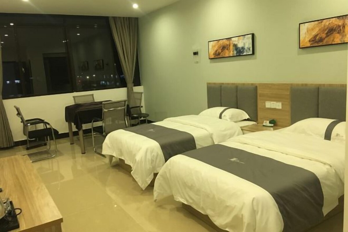 A hotel room with two beds, a desk, a chair, and a view of the city at night.