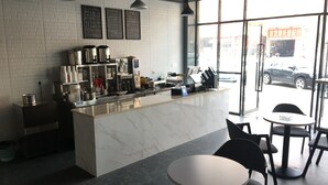 A modern cafe interior with a marble counter, black chairs, and a large window offering a view of the street. - First Apartment (Jiangmen)