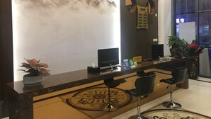 A reception desk with two computer monitors, a potted plant, and a decorative wall with a mountain painting. - First Apartment (Jiangmen)
