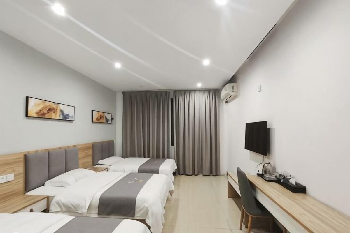 A hotel room with three beds, a desk, a TV, and two paintings on the wall.