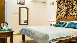 A hotel room with a bed, a bedside table with a kettle and cups, a lamp, a mirror, and a patterned curtain. - Eve Resort (Canacona)