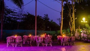 An outdoor dining area with wicker chairs and tables, surrounded by trees and a street lamp. - Eve Resort (Canacona)