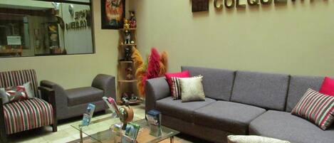 A hotel lobby with a sofa, chairs, a coffee table, and a wall sign that reads "HOTEL COLQUEWA".