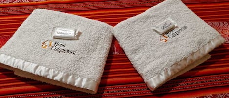 Dos toallas blancas con el logo del hotel sobre un tejido rojo estampado.
