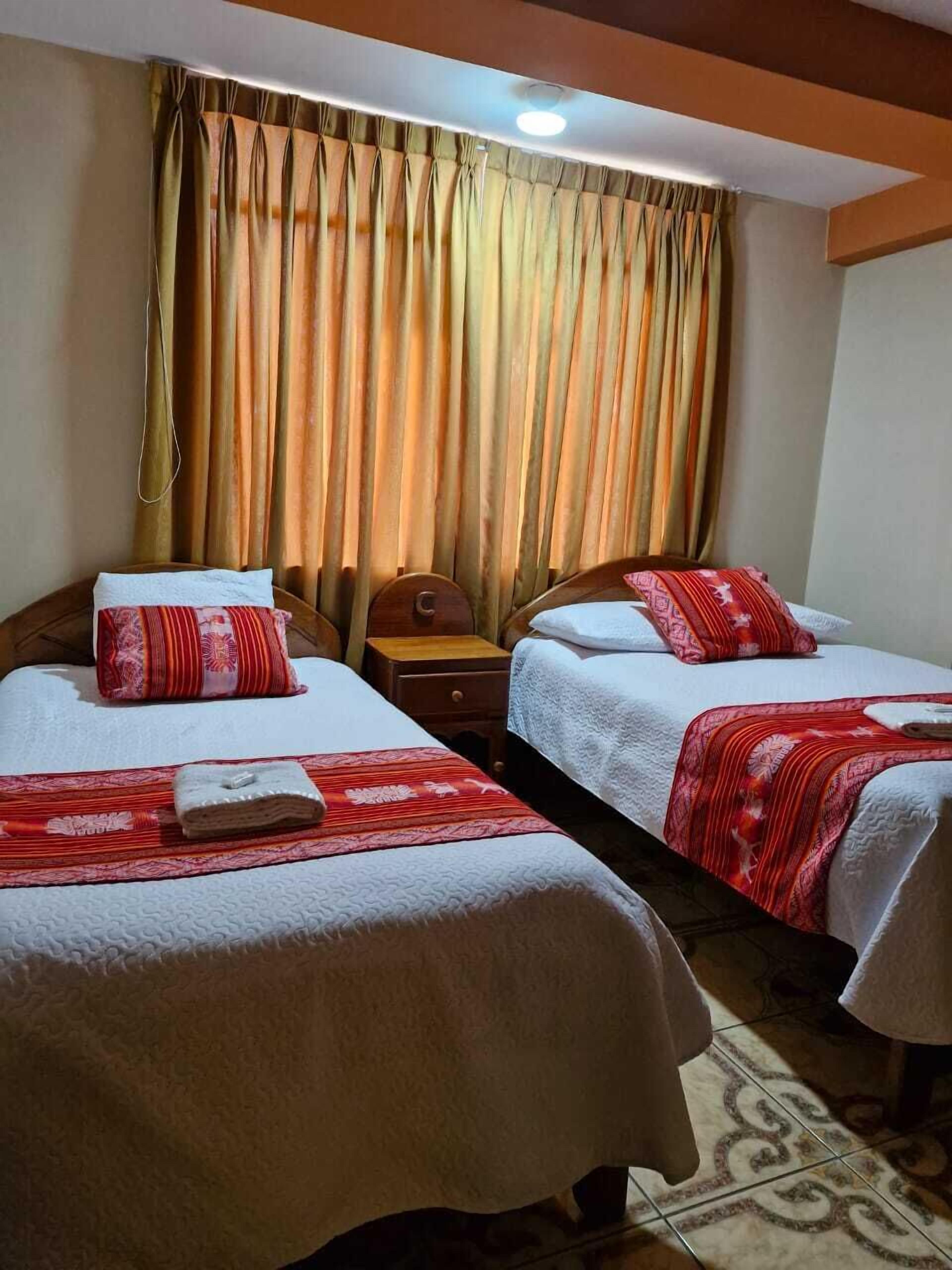 A hotel room with two beds, a wooden headboard, a nightstand, and a window with curtains.