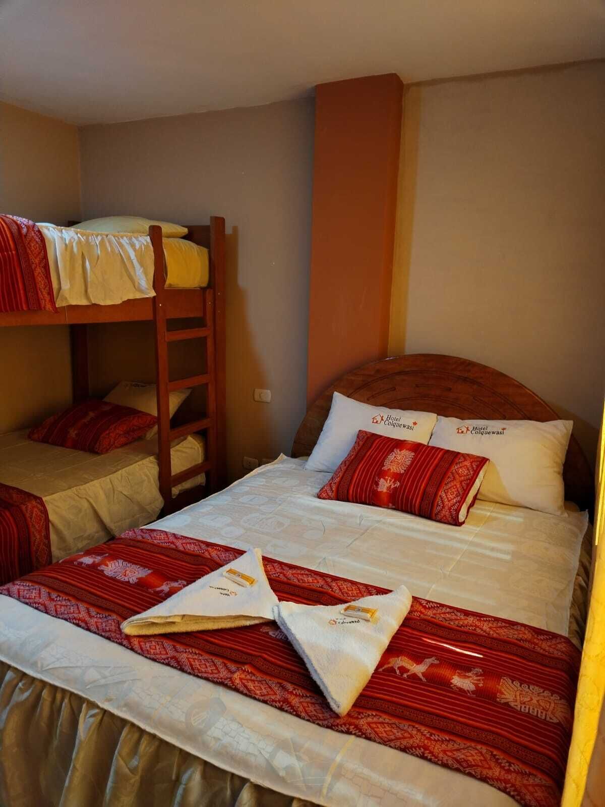 A dormitory room with bunk beds, a wooden ladder, and a bed with red and white bedding.