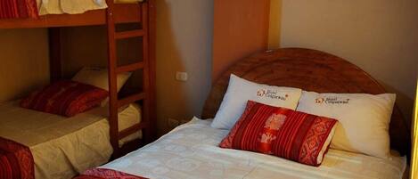 A dormitory room with bunk beds, a wooden ladder, and a bed with red and white bedding.