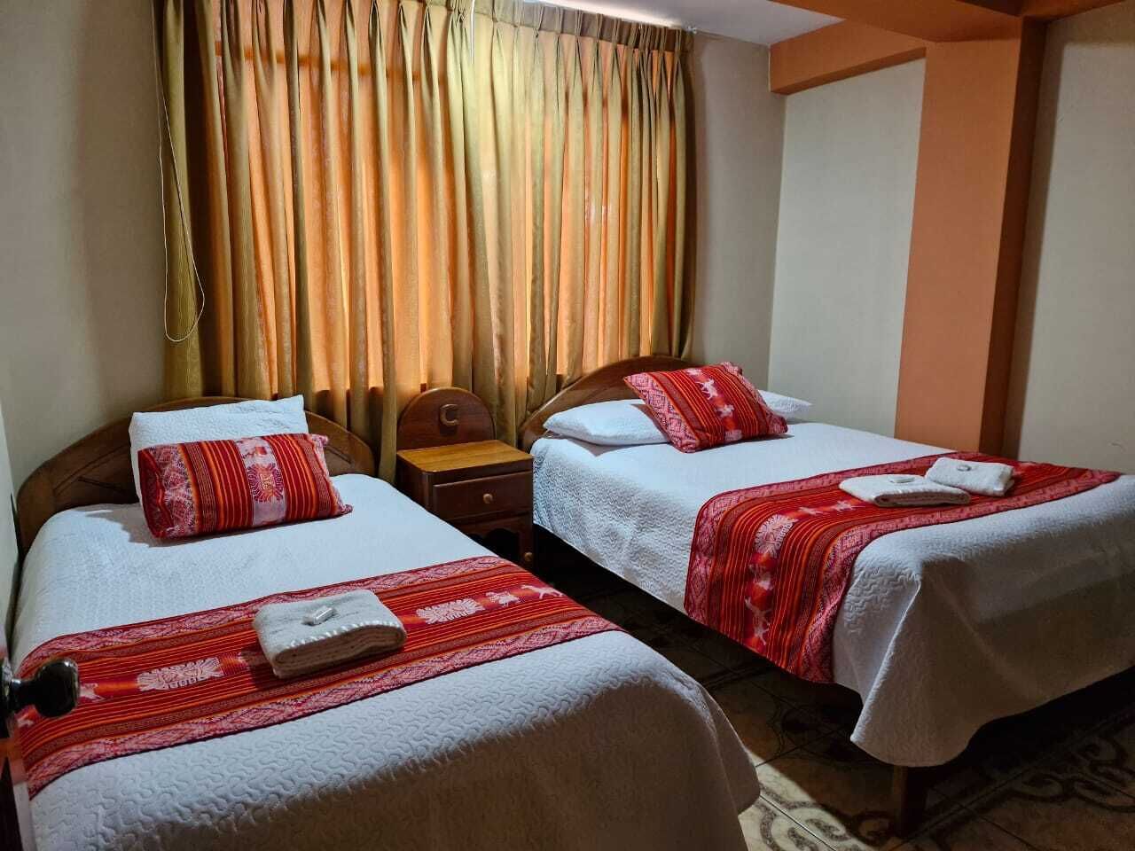 Een hotelkamer met twee bedden, elk met witte beddengoed en rode accenten, een houten hoofdeinde en een nachtkastje met een lamp.