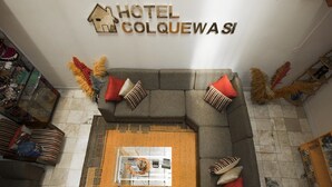A hotel lobby with a gray sectional sofa, a coffee table, and a sign reading "HOTEL COLQUEWASI". - Hotel Colquewasi (Cusco)