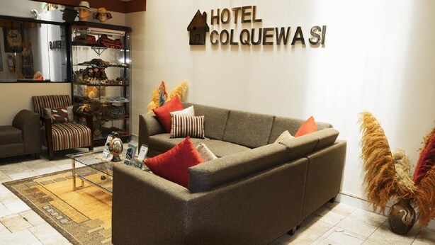 A living room with a sofa, armchairs, a coffee table, and a bookshelf. A sign above reads "HOTEL COLQUEWA SI". - Hotel Colquewasi (Cusco)