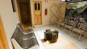 A hotel lobby with a reception desk, a waiting area with a sofa and chairs, a fire extinguisher, and a wall with a mural. - Hotel Colquewasi (Cusco)