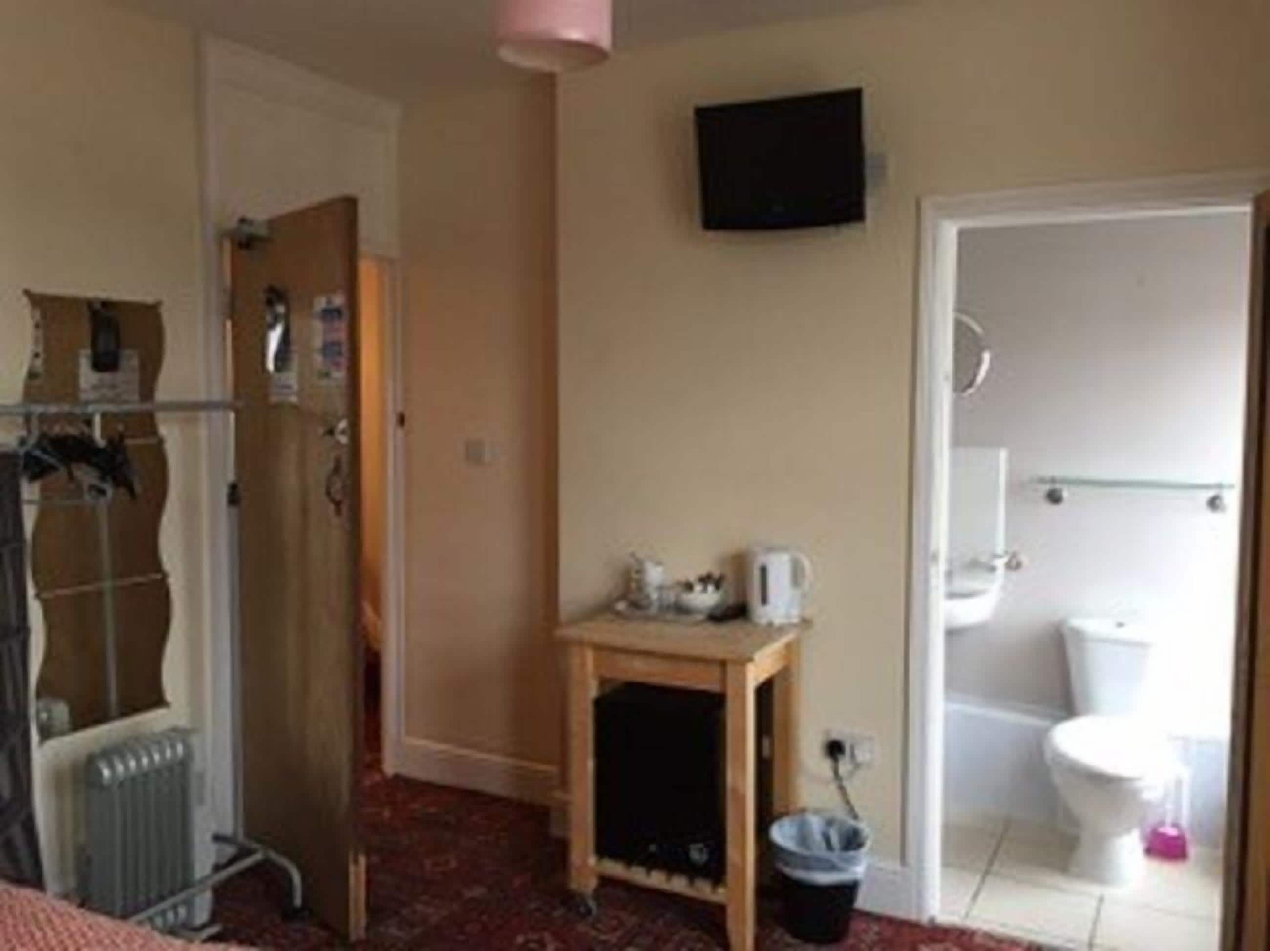 A room with a radiator, a wooden table with a kettle, a television on the wall, and a bathroom with a toilet and a bidet.