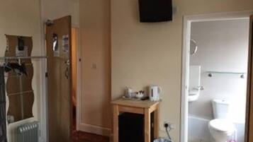 A room with a radiator, a wooden table with a kettle, a television on the wall, and a bathroom with a toilet and a bidet.