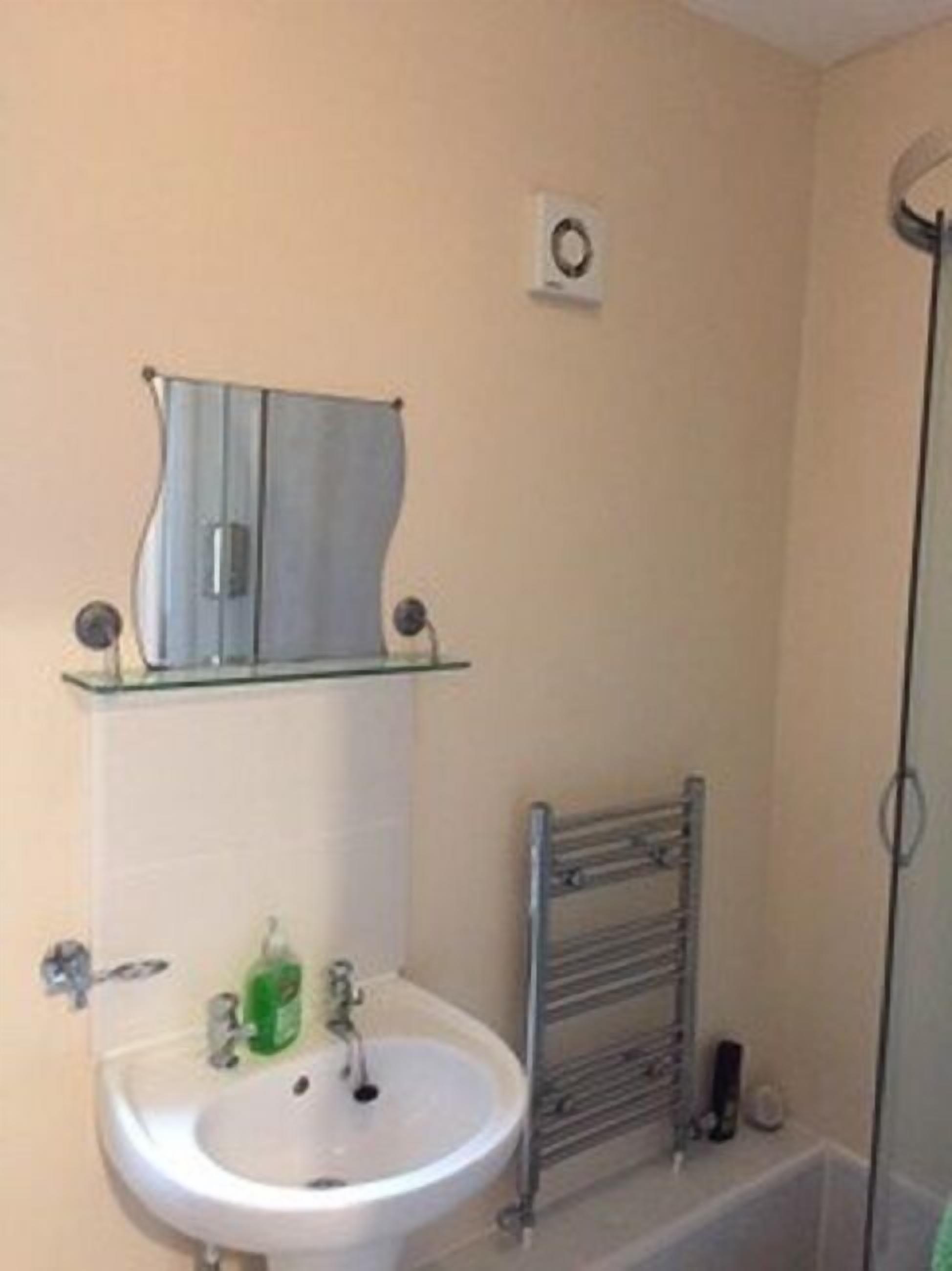 A bathroom with a white sink, a glass shower enclosure, a towel rack, and a small shelf with a mirror.