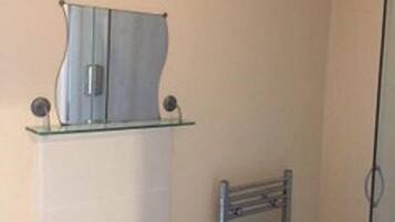 A bathroom with a white sink, a glass shower enclosure, a towel rack, and a small shelf with a mirror.