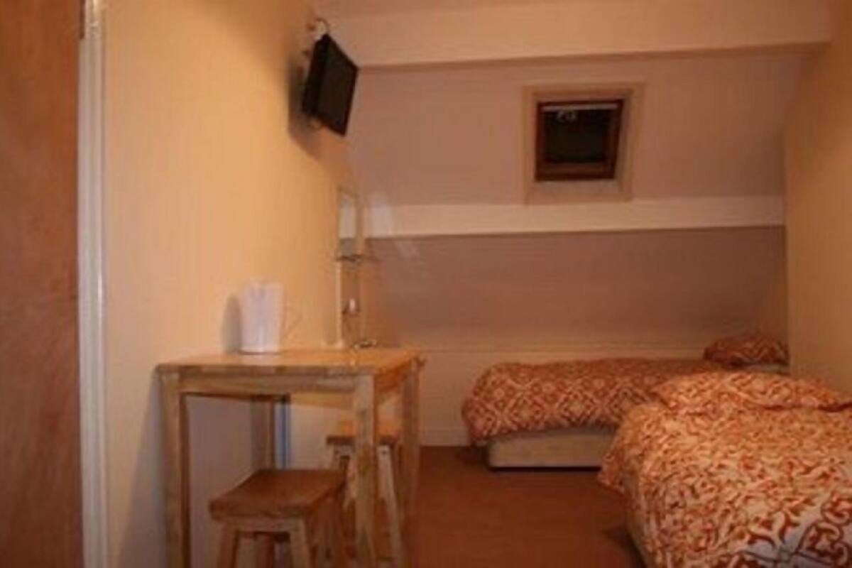 A small, compact room with two beds, a small table, and a TV mounted on the wall.