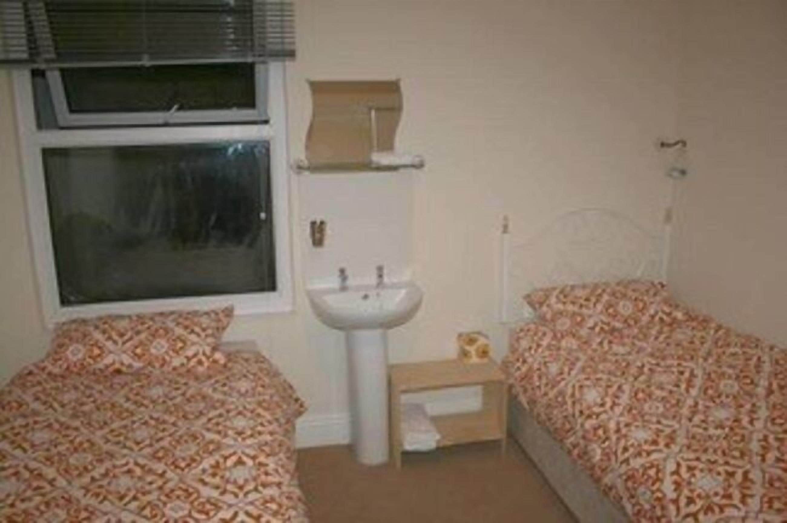 A small, single-room bedroom with two beds, a window, a sink, and a mirror.