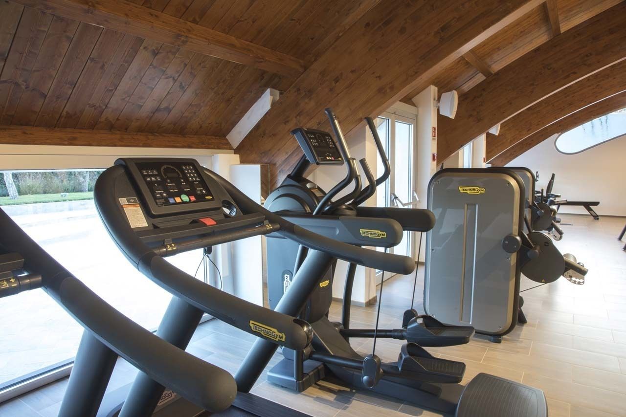 A gym with treadmills and an elliptical machine, wooden ceiling beams, and large windows.