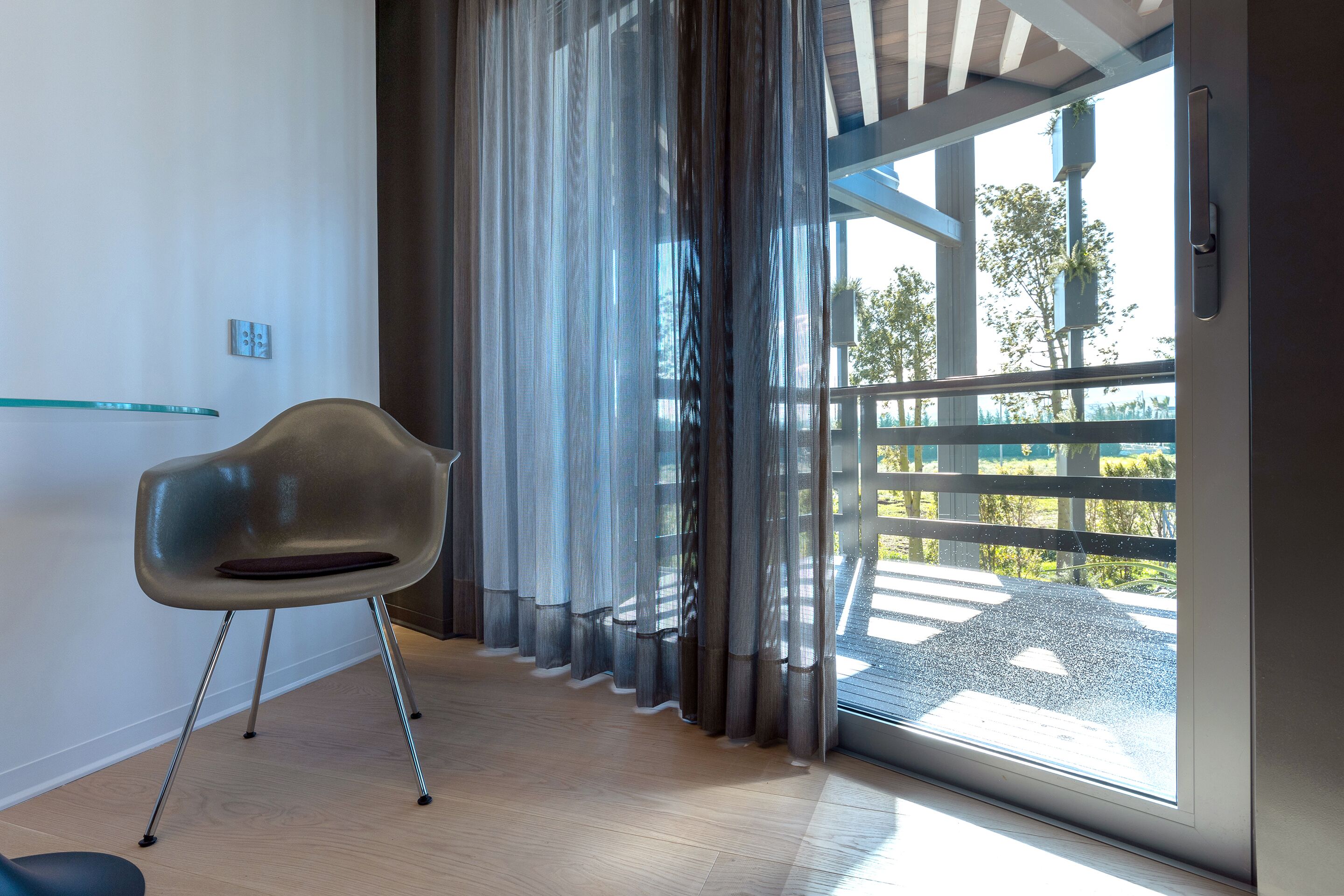 A modern room with a large sliding glass door, a contemporary chair, and a glass shelf.