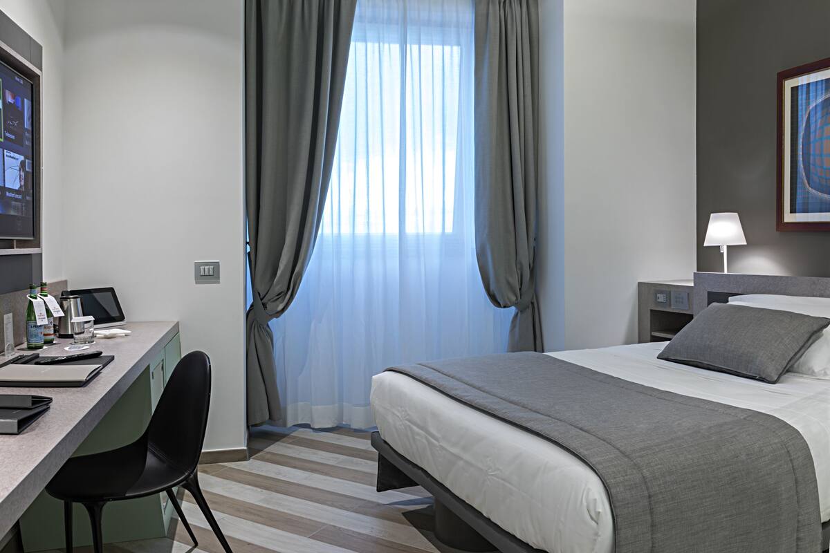 A hotel room with a bed, desk, chair, and curtains.