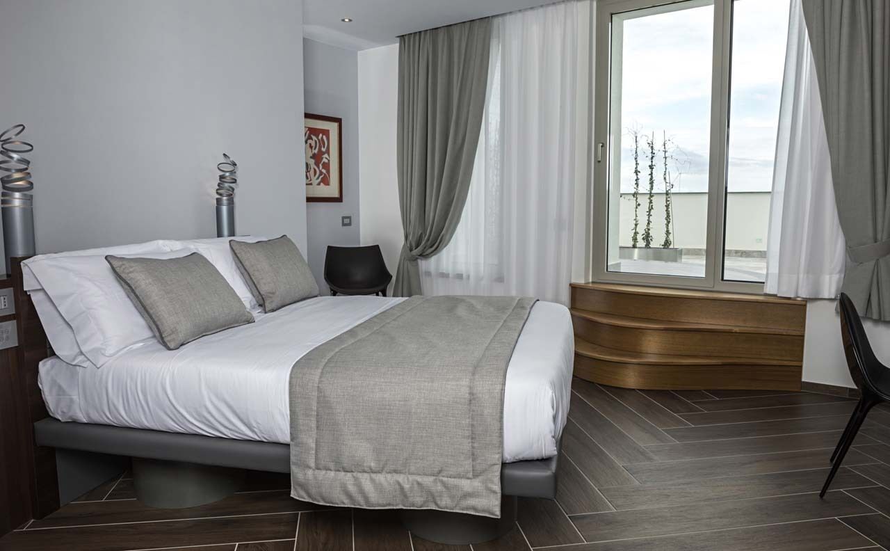 A modern bedroom with a bed, a window with curtains, a chair, and a wooden bench.
