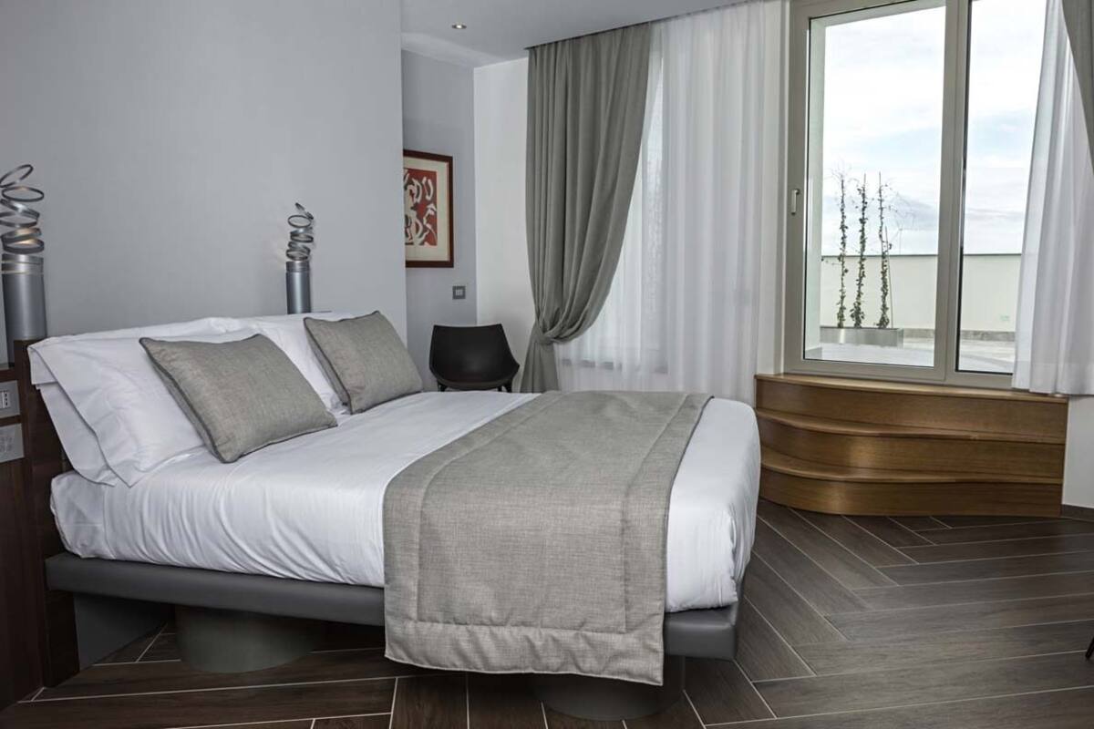 A modern bedroom with a bed, a window with curtains, a chair, and a wooden bench.