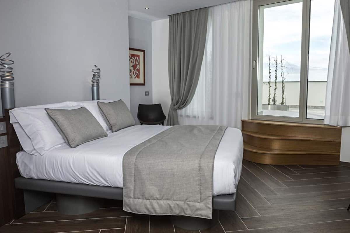 Un dormitorio moderno con cama, ventana con cortinas, una silla y un banco de madera.