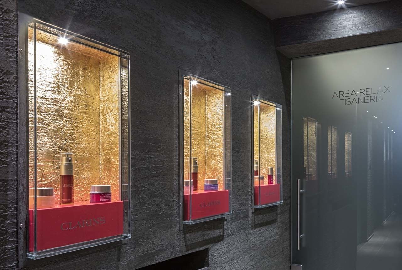 Un corridoio con tre teche illuminate con prodotti per la cura della pelle, etichettate 'CLARINS'.