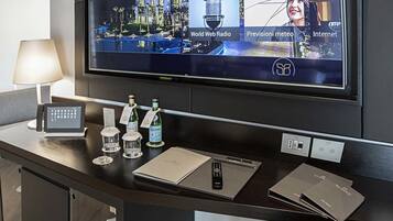 A hotel reception desk with a large screen displaying various channels, a control panel, and amenities like bottled water and a remote control.