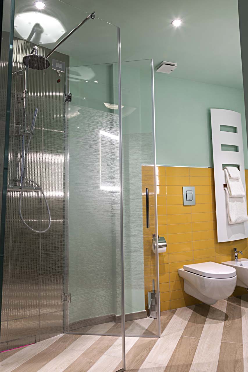 Un baño moderno con ducha envuelta en vidrio, un lavamanos blanco y una pared con azulejos amarillos.