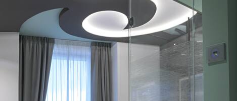 Una habitación de hotel moderna con cama, sillón y separador de vidrio.