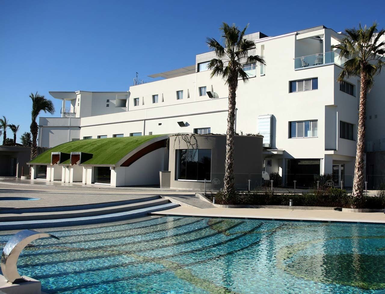 Un hotel moderno con piscina, palmeras y fachada de vidrio curva.