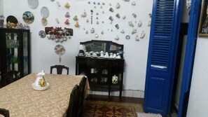 Un coin repas avec une table dressée pour deux personnes, un meuble avec des portes en verre et un mur décoré de divers objets en céramique.