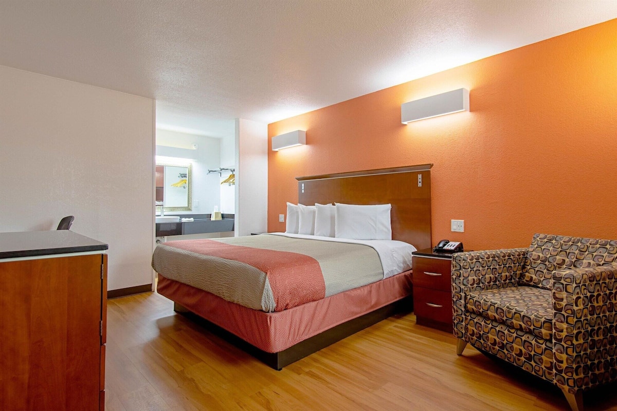 A hotel room with a bed, bedside table, and a patterned armchair.