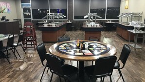 A modern restaurant with a central round table surrounded by chairs, a buffet area, and a bar.