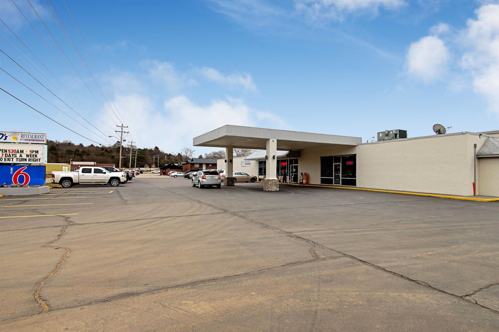 A gas station with a large canopy, a restaurant sign, and a parking lot with several cars.