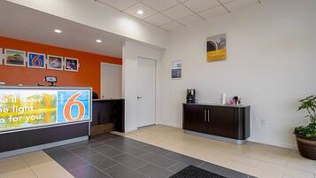 A hotel reception area with a counter, a coffee machine, a potted plant, and a sign advertising the hotel.