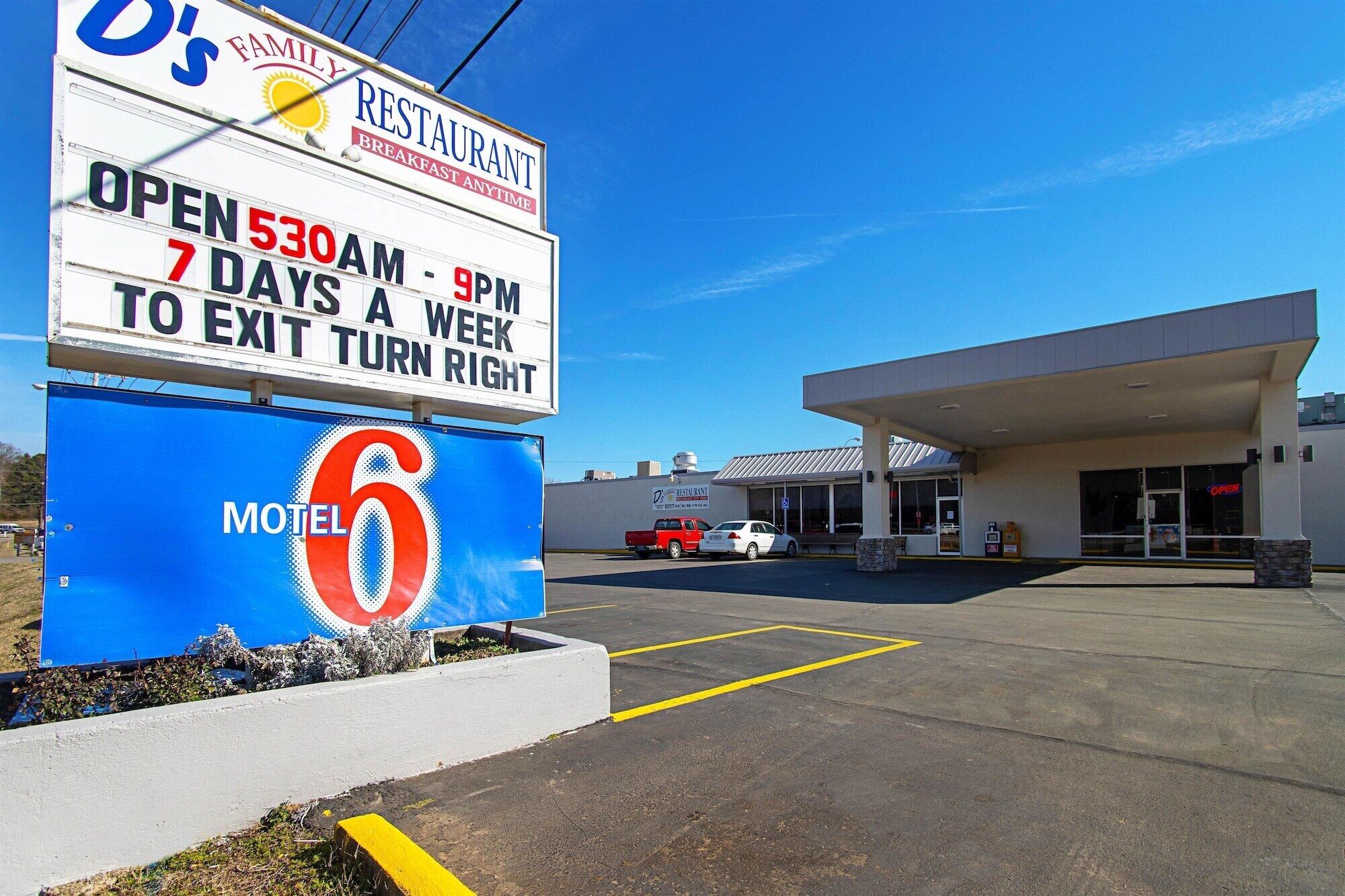 Une enseigne de motel avec le logo « 6 », une enseigne de restaurant indiquant « ouvert de 5 h 30 à 21 h, 7 jours sur 7, pour sortir, tourner à droite », et une station-service en arrière-plan.