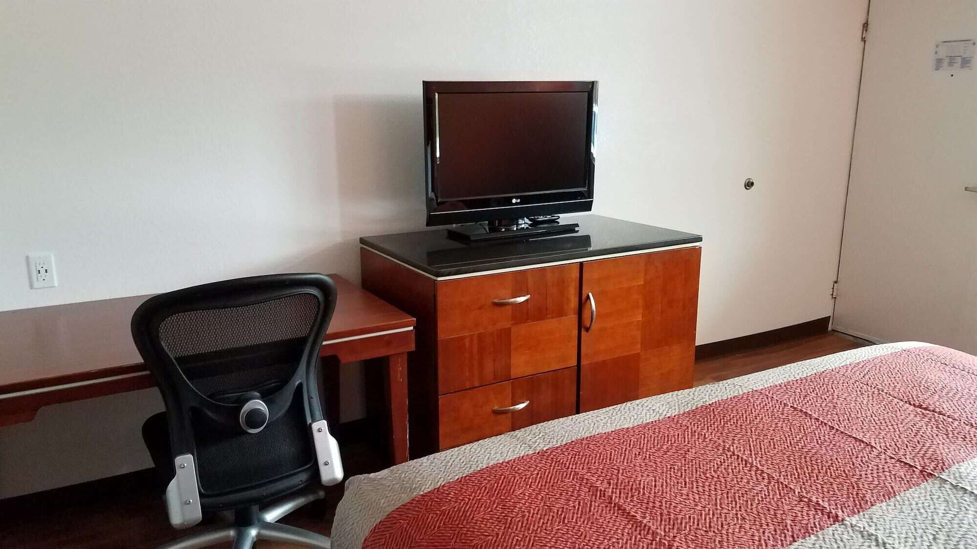 A hotel room with a bed, a desk with a chair, a TV, and a wardrobe.