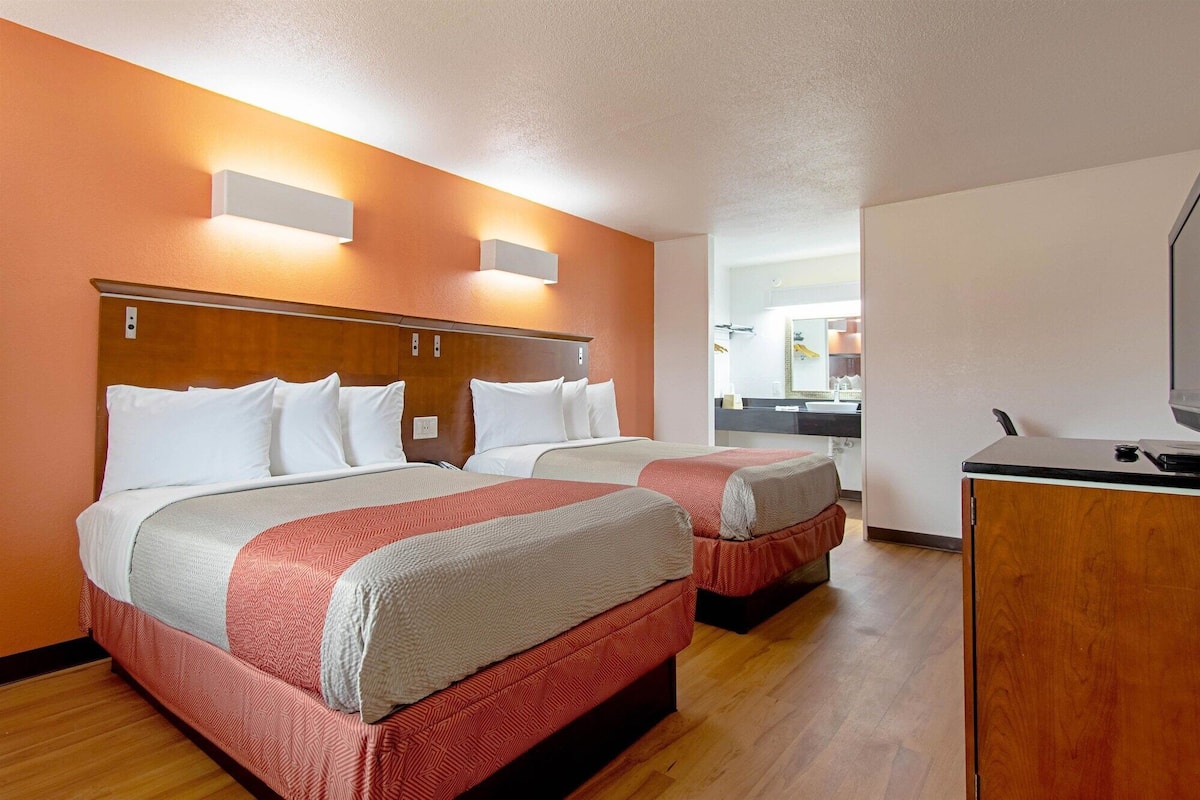 A hotel room with two beds, a desk, and a kitchenette.