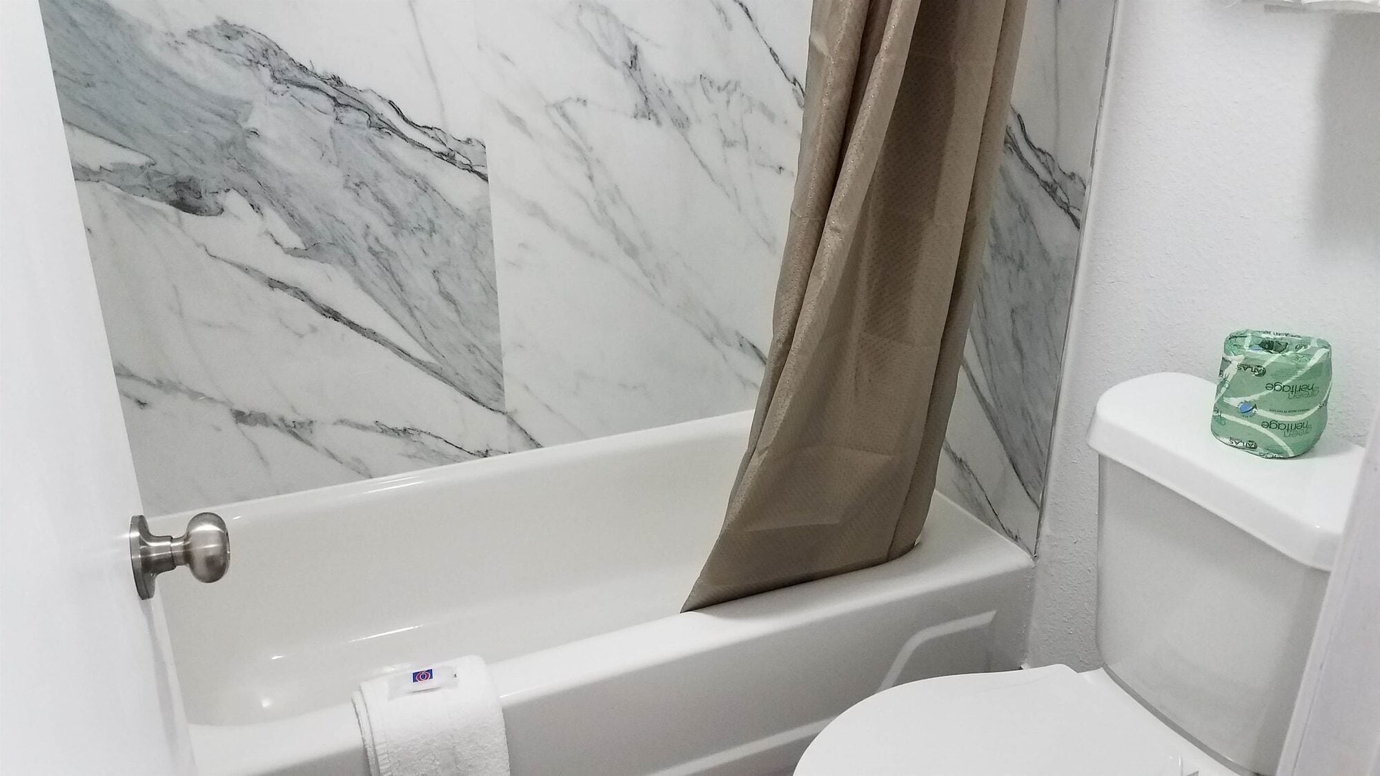A bathroom with a bathtub, toilet, and marble wall.