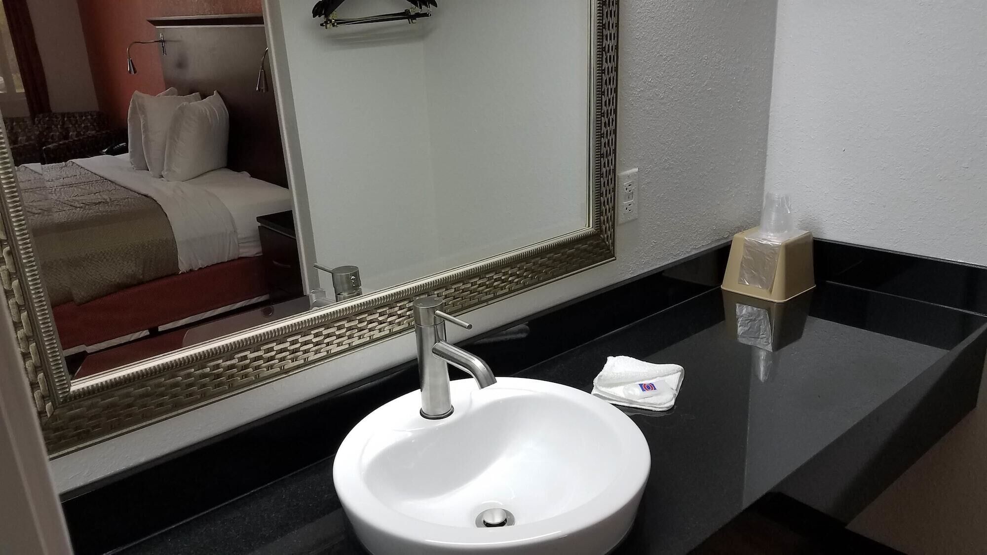 A bathroom with a white sink, a mirror, and a black countertop.