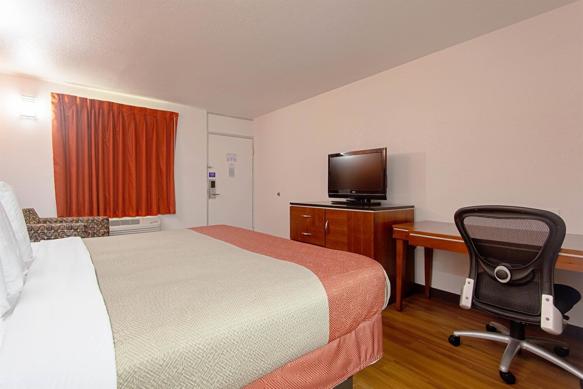 A hotel room with a bed, a desk with a television, and a chair.