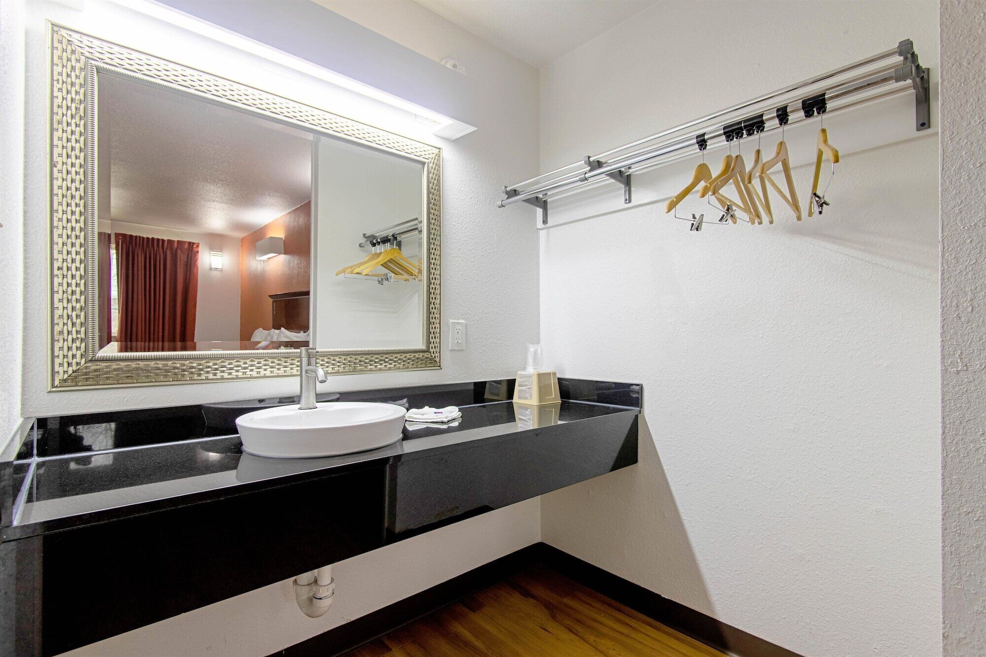A modern bathroom with a large mirror, a round sink, and a towel rack with hangers.