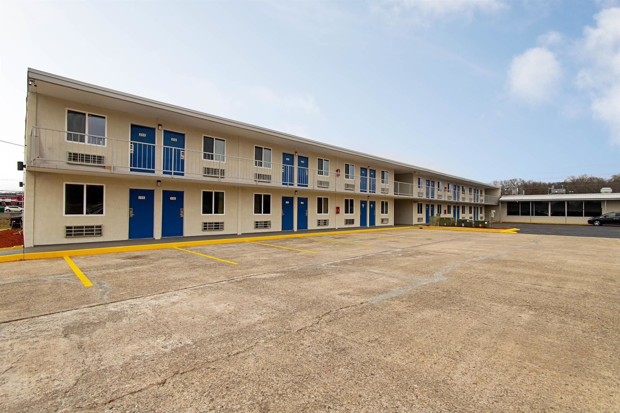Un motel con una hilera de habitaciones, cada una con una puerta azul y un pequeño balcón.