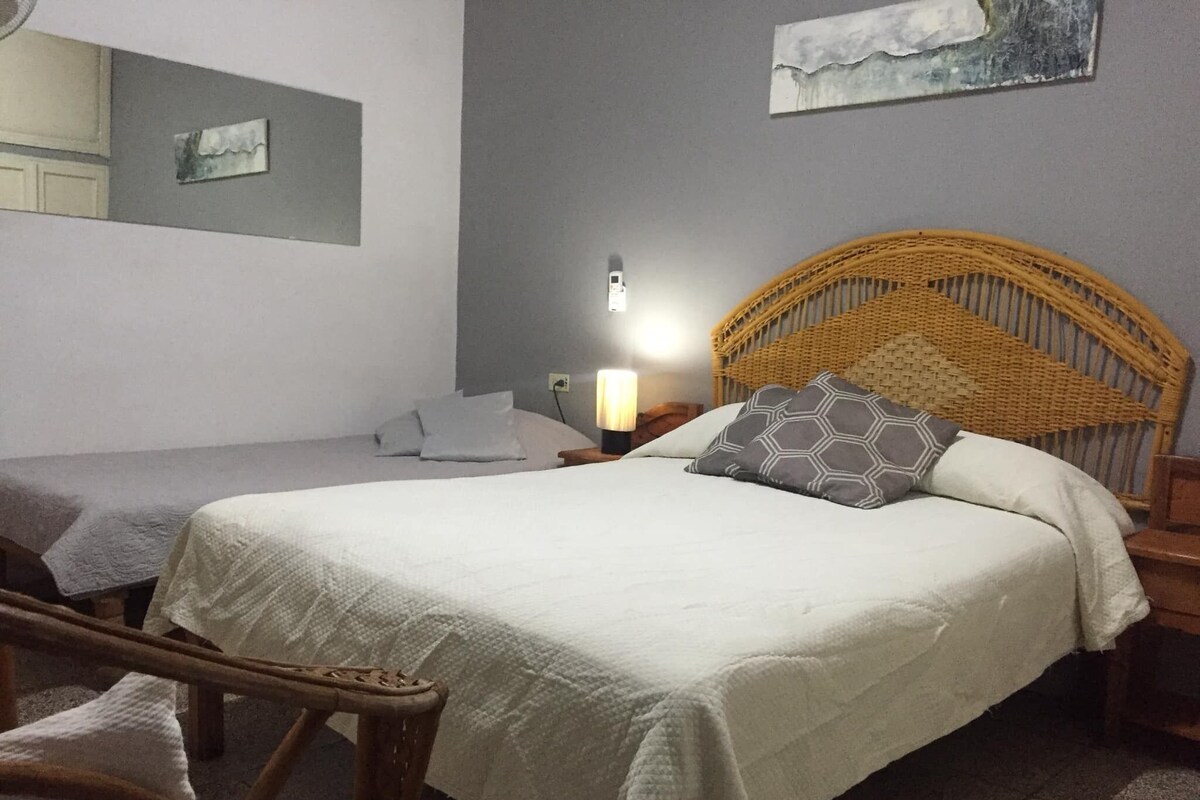 A bedroom with a large bed, a smaller bed, a wicker headboard, and a nightstand with a lamp.