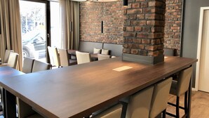 A modern dining area with a long wooden table, cushioned chairs, and a brick accent wall. - Rafaela Hotel Heidelberg (Heidelberg)
